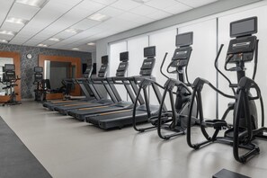 Une salle de sport dotée de plusieurs tapis de course, d’appareils elliptiques et de vélos d’exercice, et équipée d’écrans numériques et de panneaux de commande.