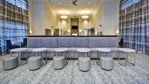 Eine Lobby mit einer Sitzecke, runden Tischen und einer zentralen Säule mit einem Fernseher.