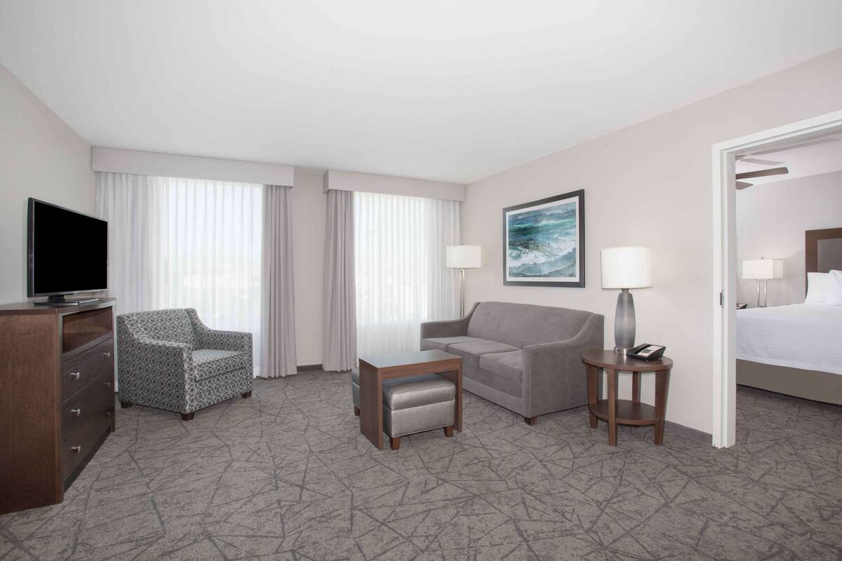 Habitación de hotel con televisión de pantalla plana, un sillón estampado, un sofá, una mesita con lámpara y una cama.