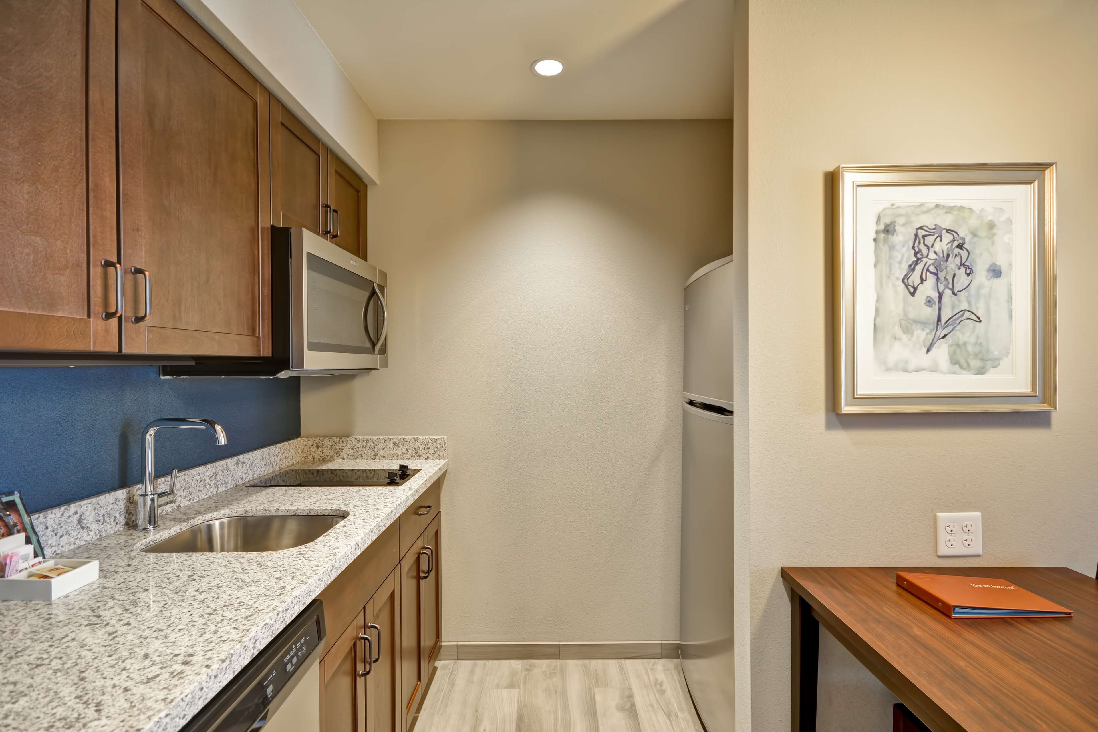 A kitchen with granite countertops, stainless steel appliances, wooden cabinets, and a framed artwork on the wall.