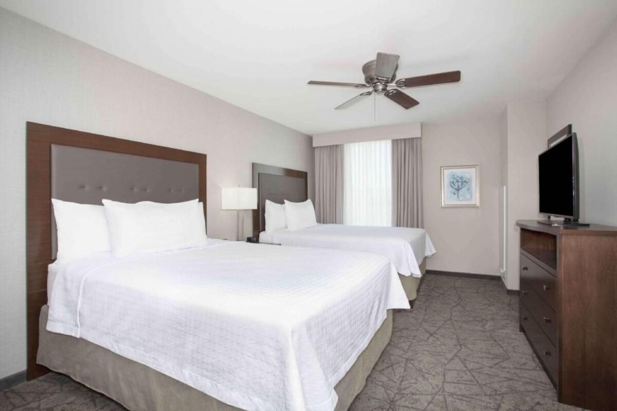A hotel room with two beds, a ceiling fan, a TV, and a dresser.