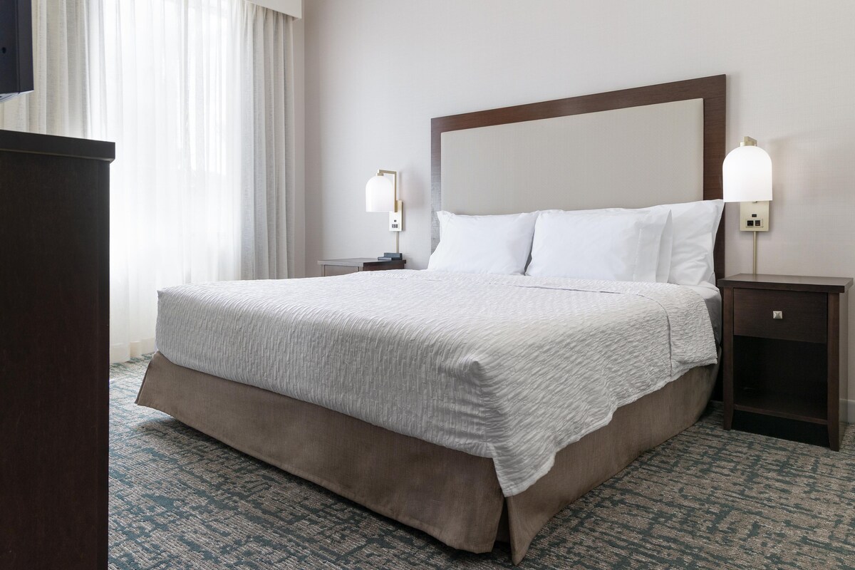 Une chambre d’hôtel avec un grand lit, deux tables de chevet, une petite table et une lampe fixée au mur.