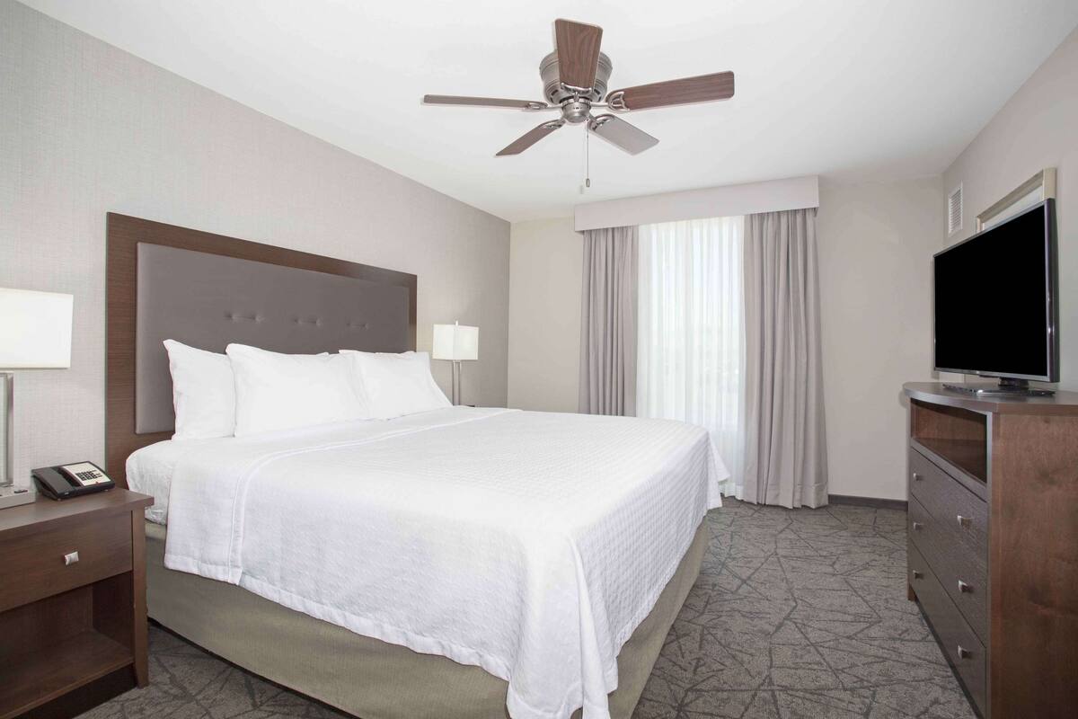 Una habitación de hotel con una cama grande, un ventilador de techo, un televisor y un escritorio con teléfono.