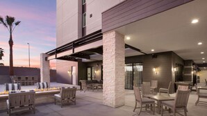 Ein Außenbereich mit Terrasse, Sitzgelegenheiten und Tischen, steinernen Säulen und einer modernen Gebäudefassade.