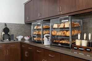 Une vitrine de boulangerie présentant diverses pâtisseries, un appareil à gaufres et une machine à café.