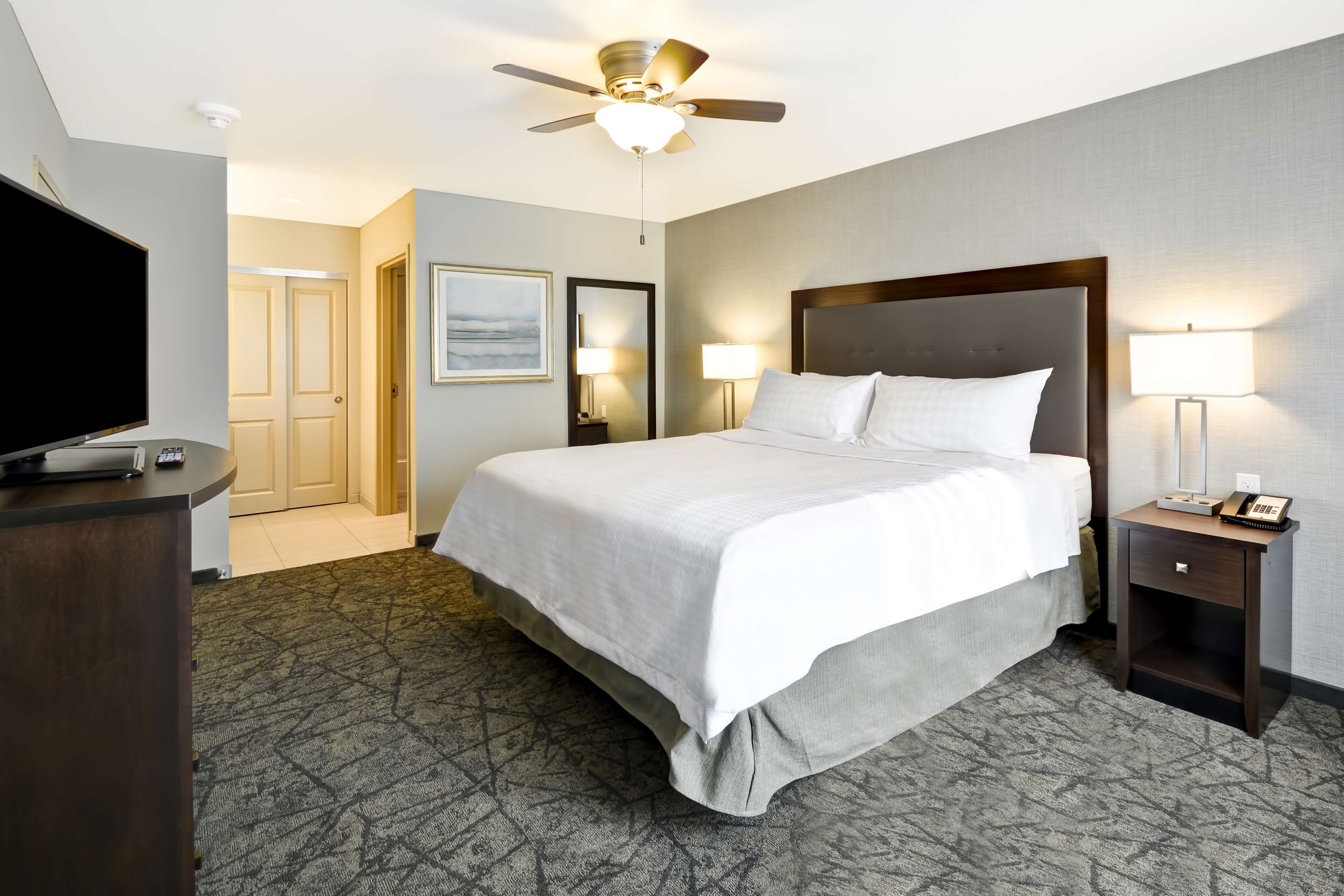 A hotel room with a large bed, a ceiling fan, a desk with a TV, and two bedside lamps.