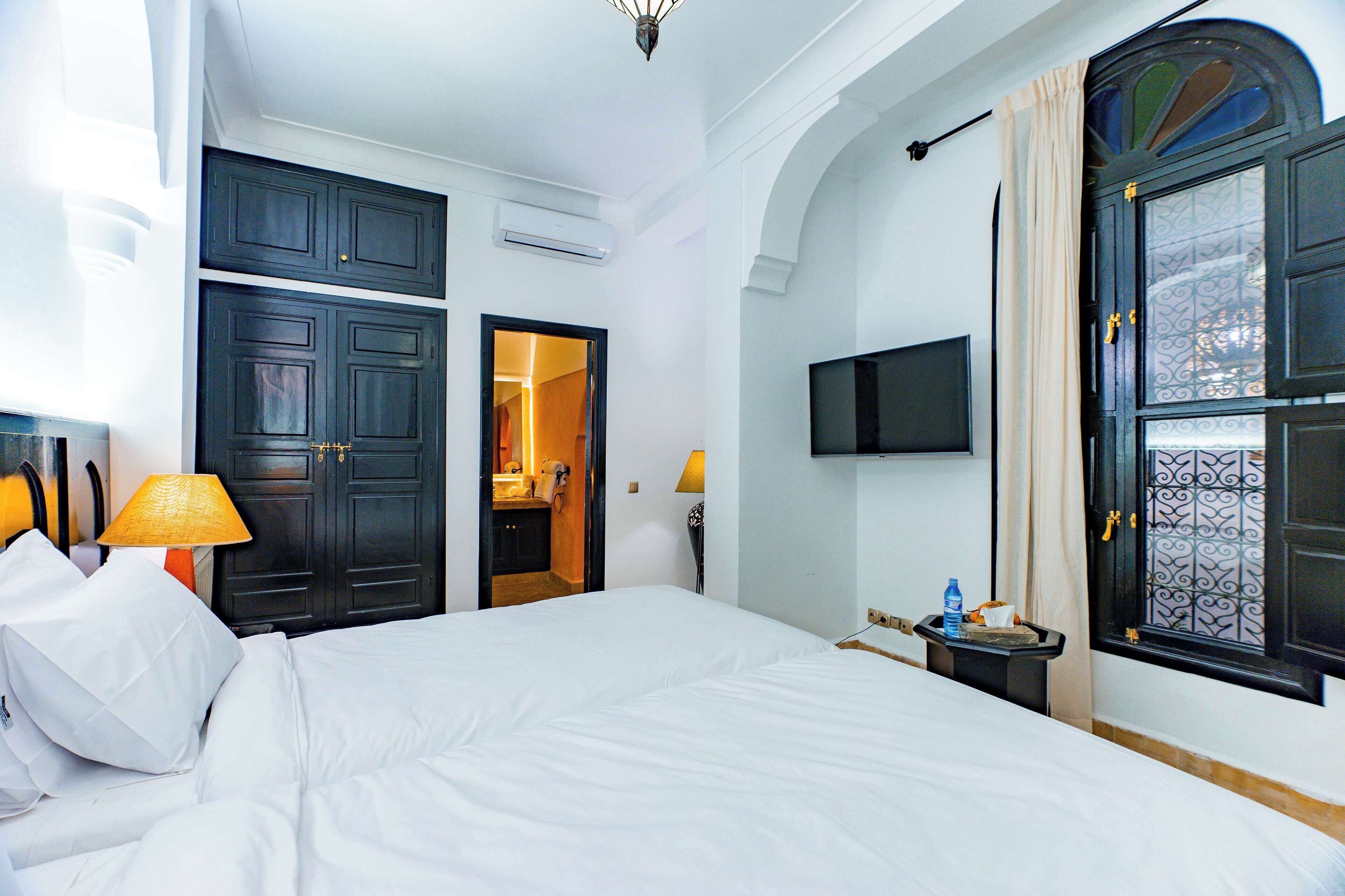 Habitació d'hotel amb un llit, una televisió penjada a la paret i una finestra amb reixa decorativa.