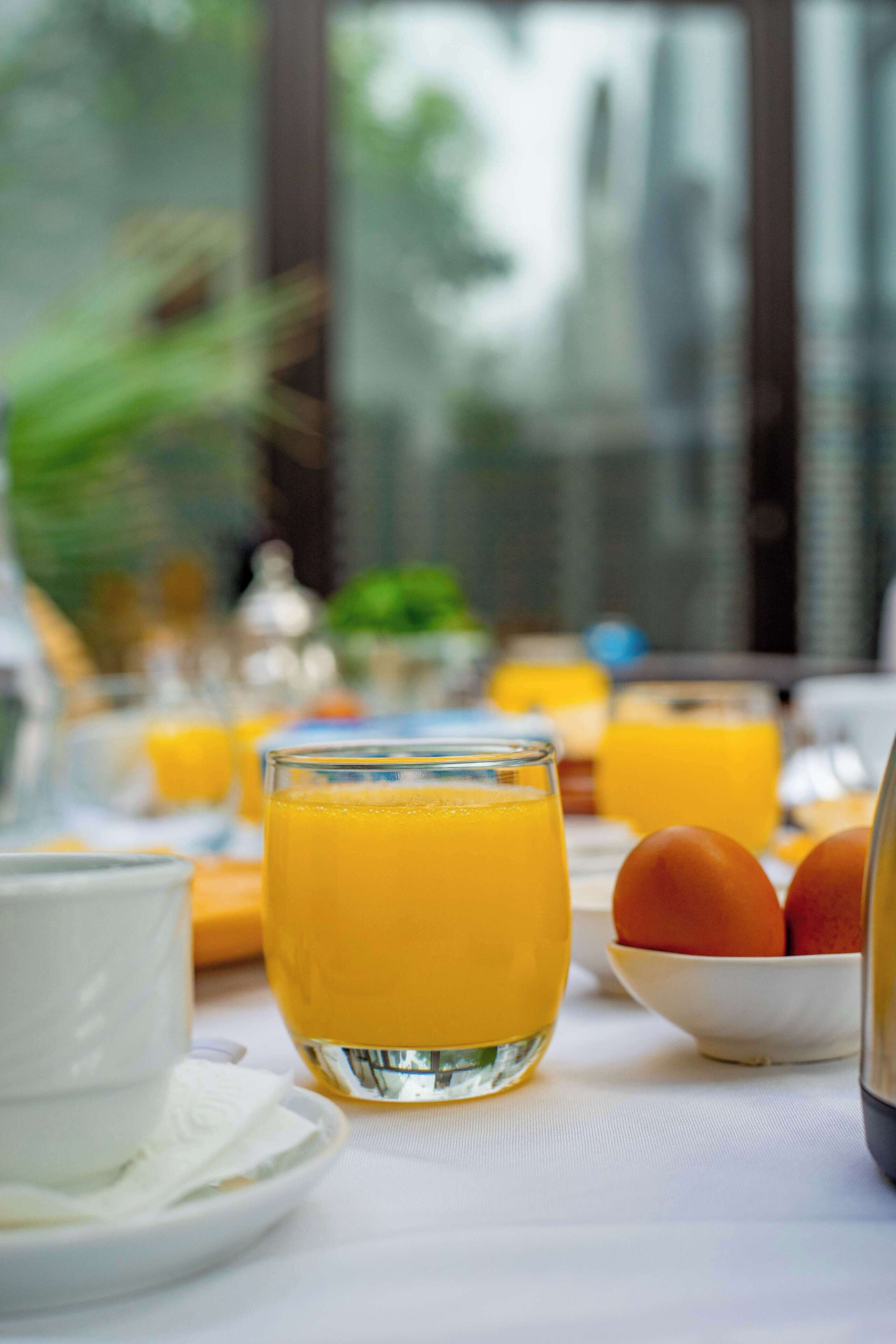 Una mesa de desayuno con jugo de naranja, huevos y una taza blanca.