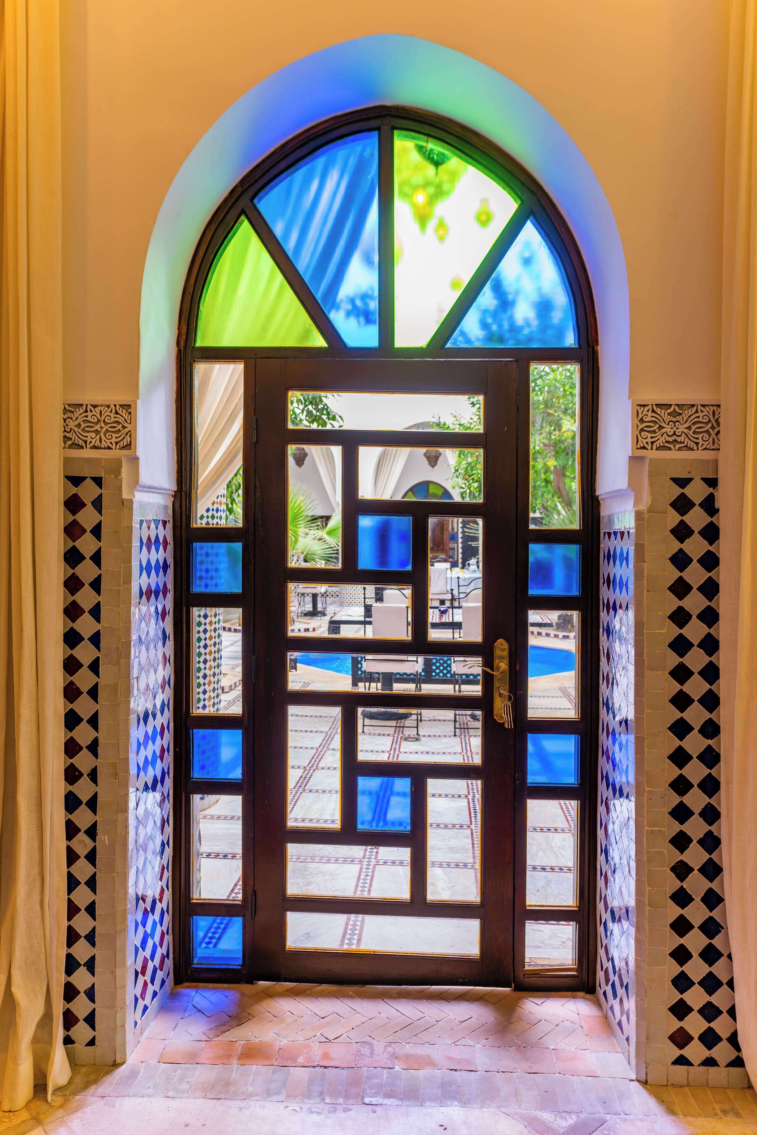 Una puerta con un diseño de vitral que da a un área exterior con piscina y asientos.