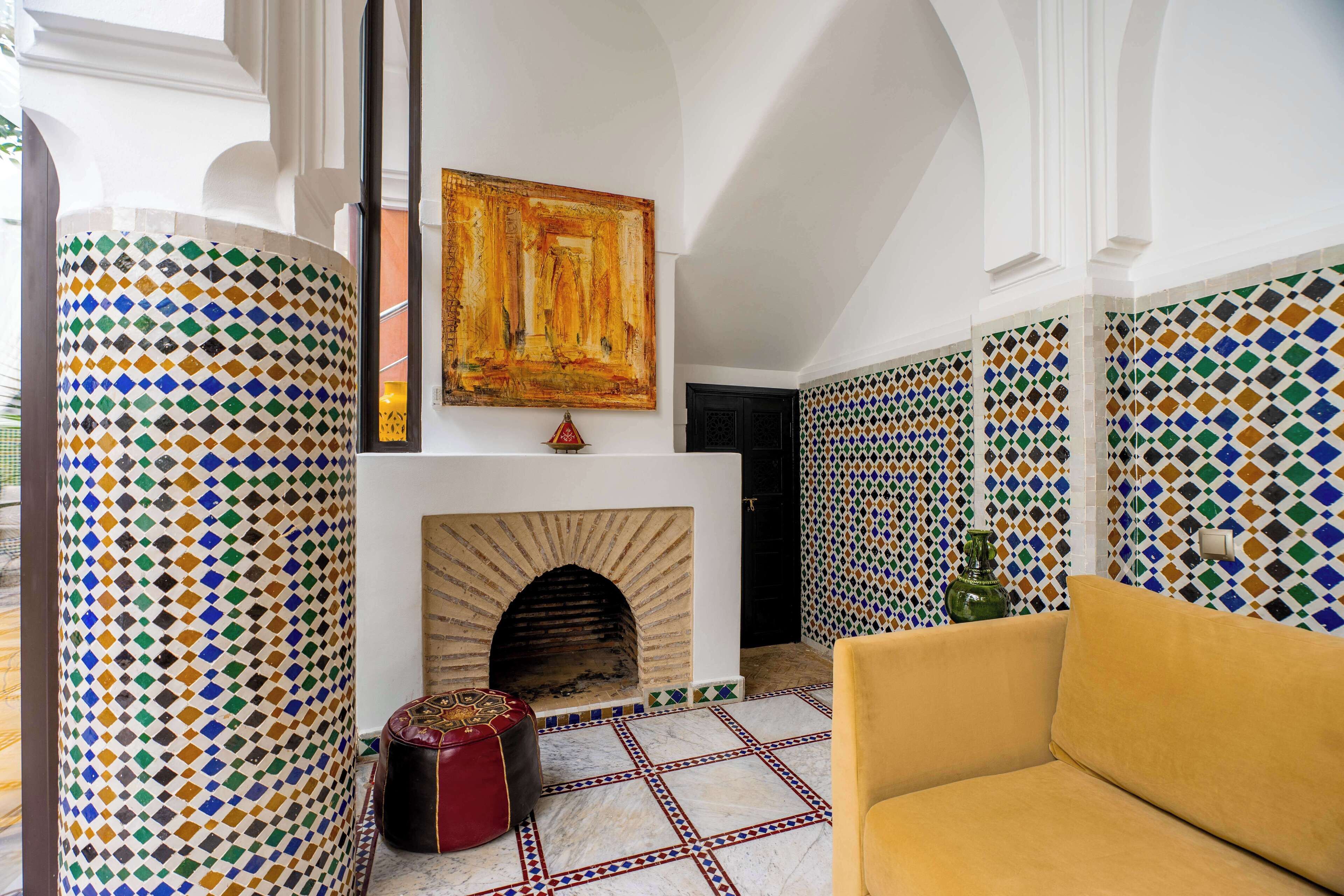 A room with a patterned floor, a fireplace, a sofa, and a wall with a large painting.