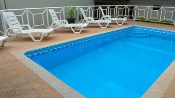 Una piscina con tumbonas blancas y un suelo de baldosas.