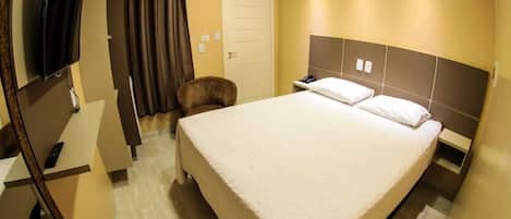 Habitación de hotel con una cama grande, un escritorio con una silla, un televisor montado en la pared y una puerta con cortinas.