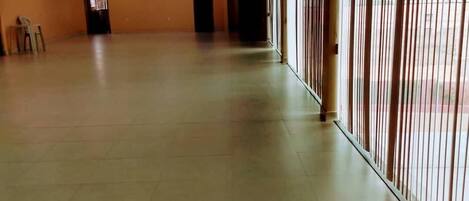 A spacious, empty room with tiled flooring, a high ceiling with recessed lighting, and large windows with vertical blinds.