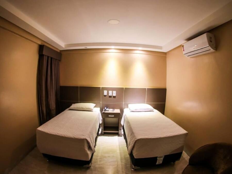 Una habitación de hotel con dos camas individuales, un escritorio, una silla y un equipo de aire acondicionado.