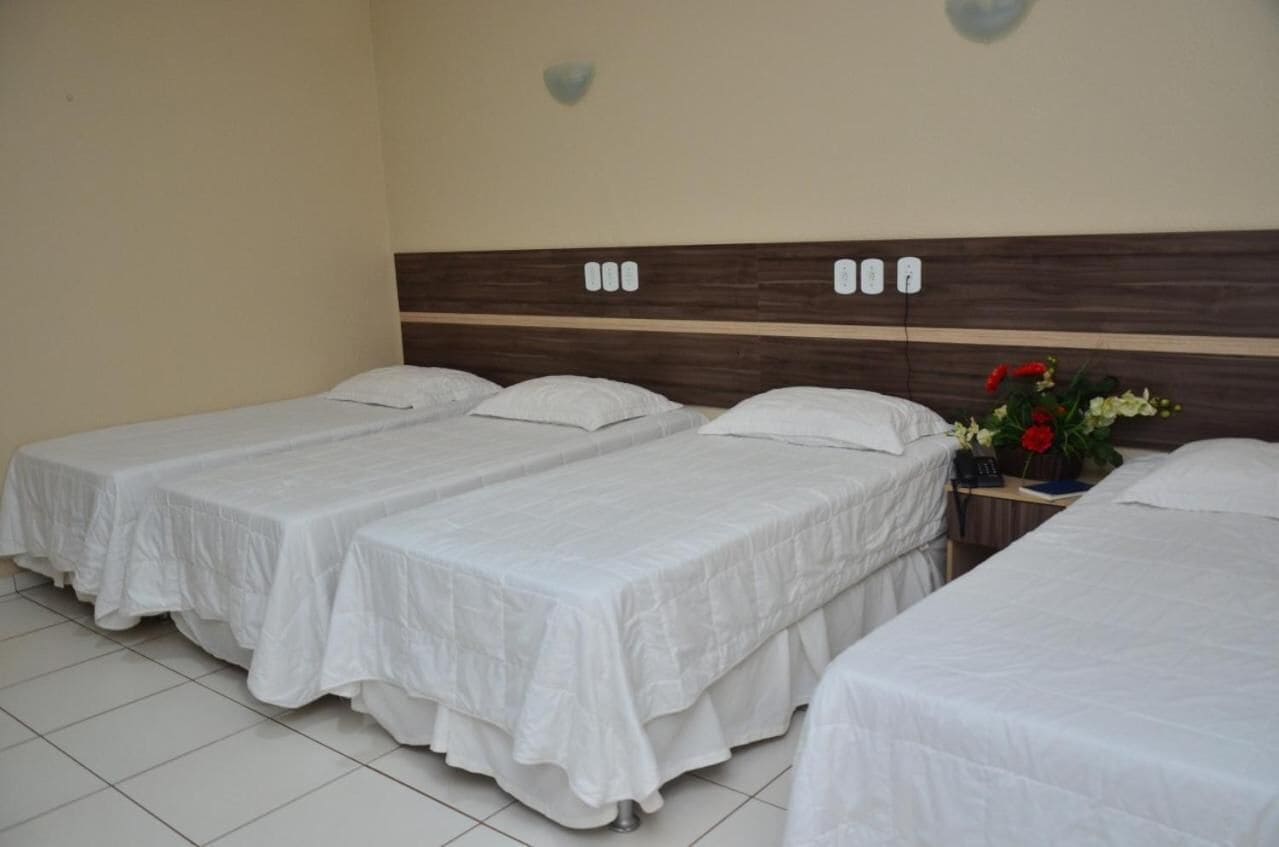 A hotel room with three single beds, a wooden headboard, and a bedside table with a vase of flowers.