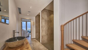 Ein modernes Badezimmer mit einem großen Steinkonfett, einer Holzablage und Blick auf eine verschneite Landschaft durch ein großes Fenster.