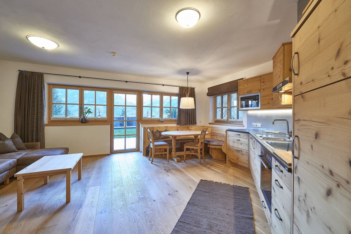 A modern kitchen with wooden cabinets, a dining area with a table and chairs, and a large window with a view of mountains.