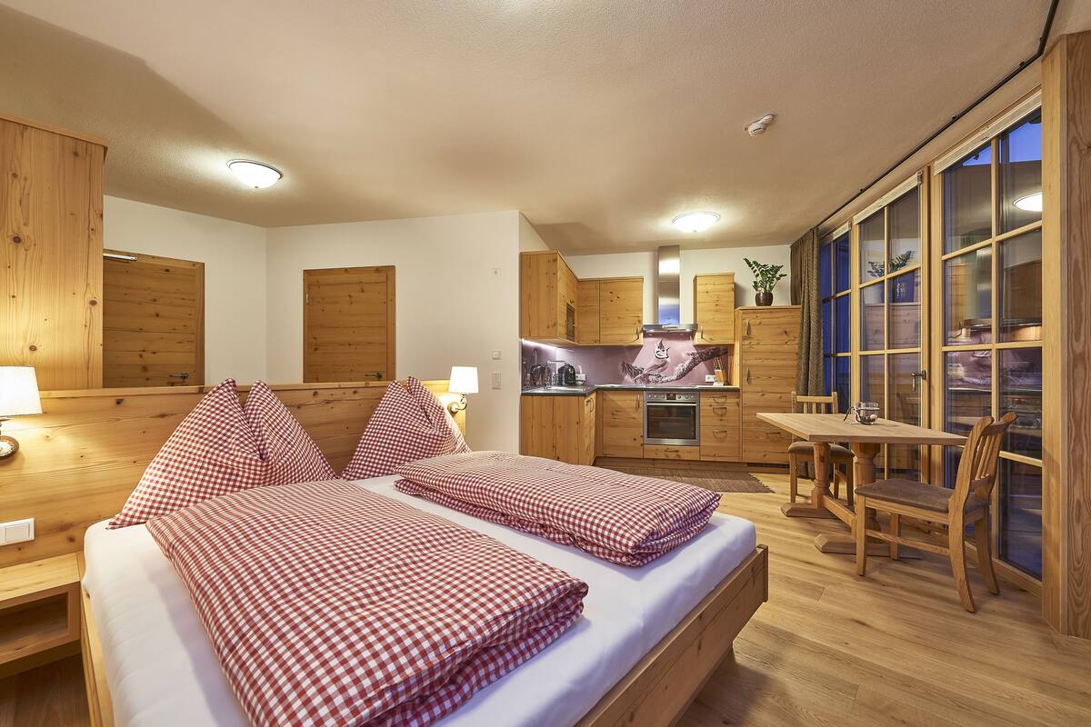 A cozy room with a bed, wooden cabinets, a small kitchen, and a dining area.