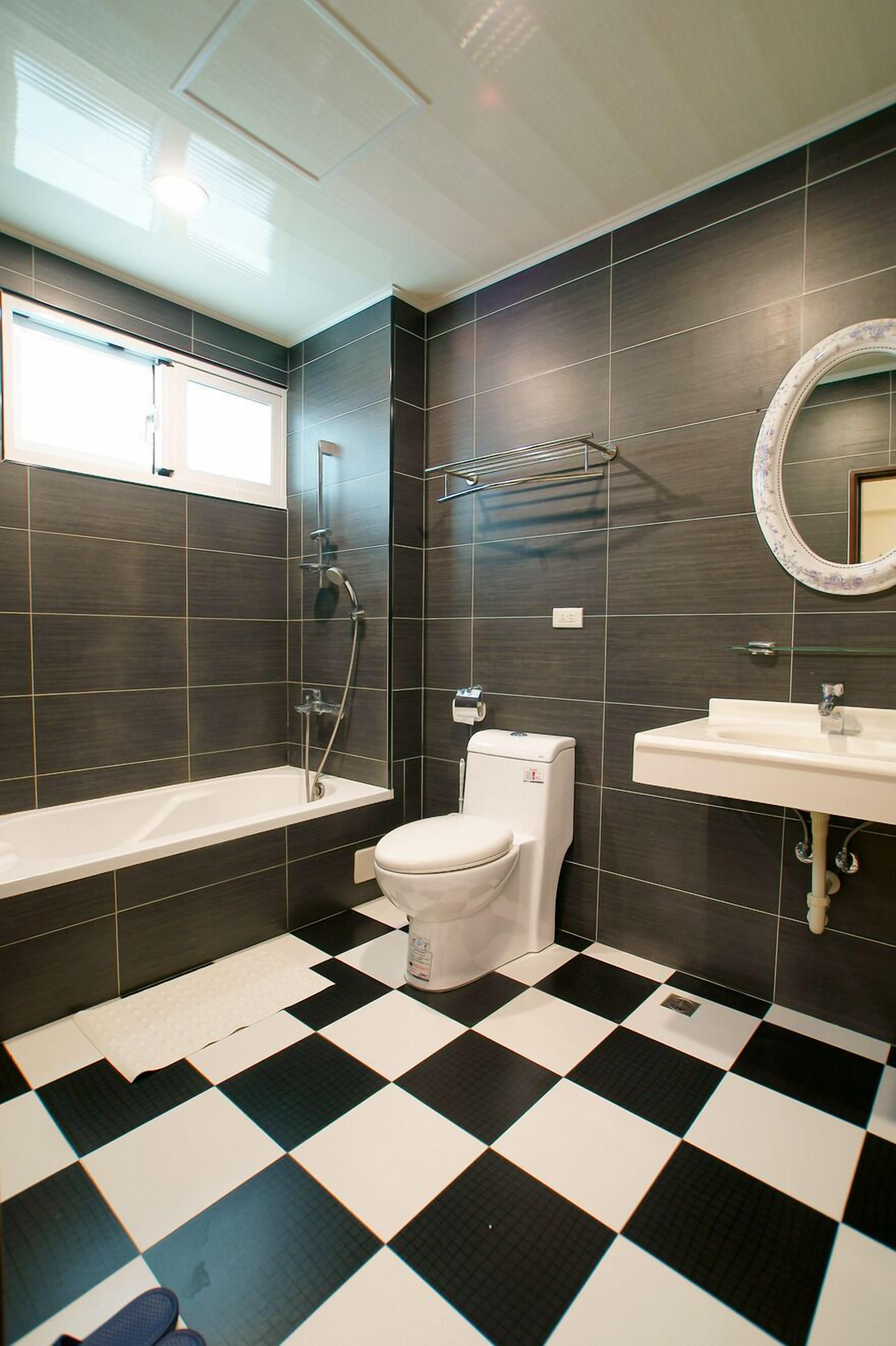 A modern bathroom with a checkered floor, a bathtub, a toilet, a sink, and a mirror.