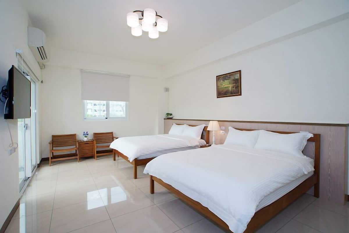 A hotel room with two beds, a TV, a window, and a painting on the wall.
