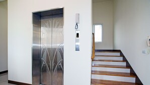 Un ascensor con puerta de vidrio decorativa, un teléfono en la pared y una escalera de madera.