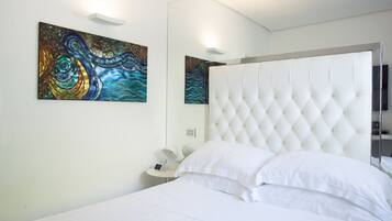 Une chambre à coucher moderne avec une tête de lit capitonnée, un lit blanc et des tableaux abstraits accrochés aux murs.