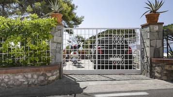 Una entrada vigilada con una reja de metal, pilares de piedra y plantas en macetas.