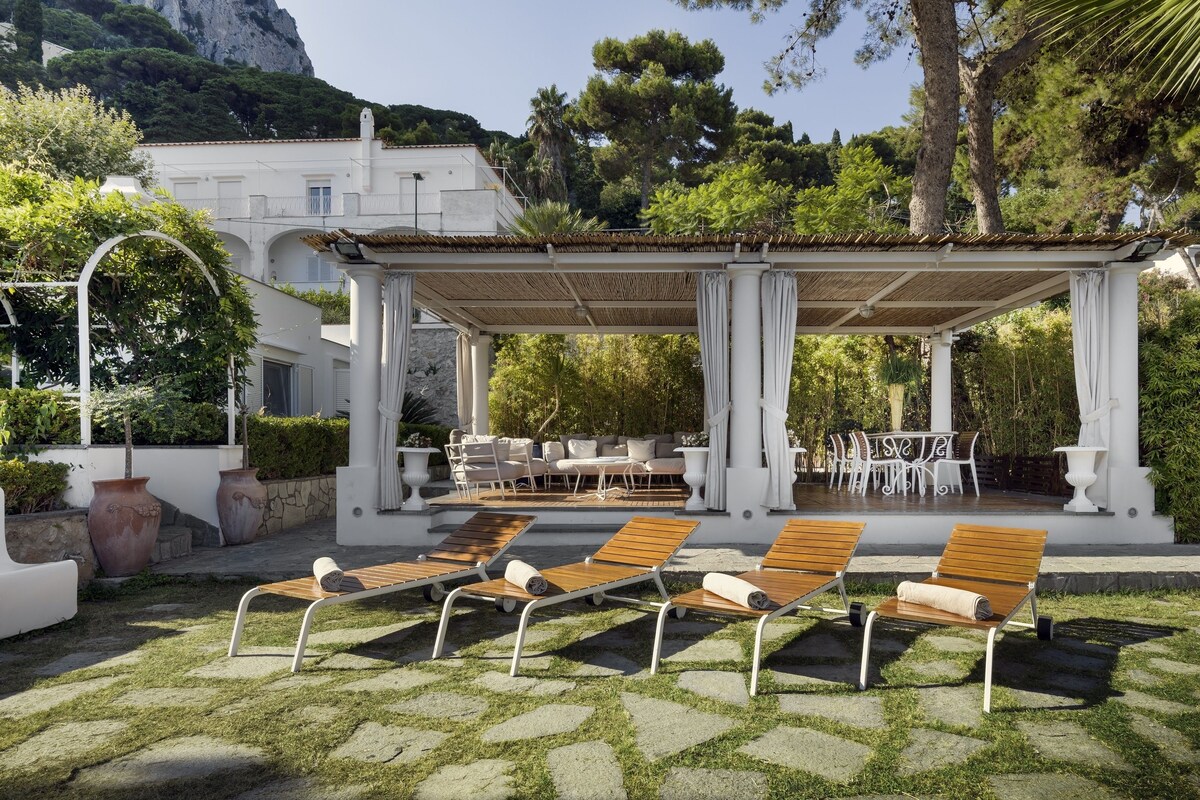 Un espacio de estar al aire libre cubierto con sillones de madera y una estructura de pérgola blanca.