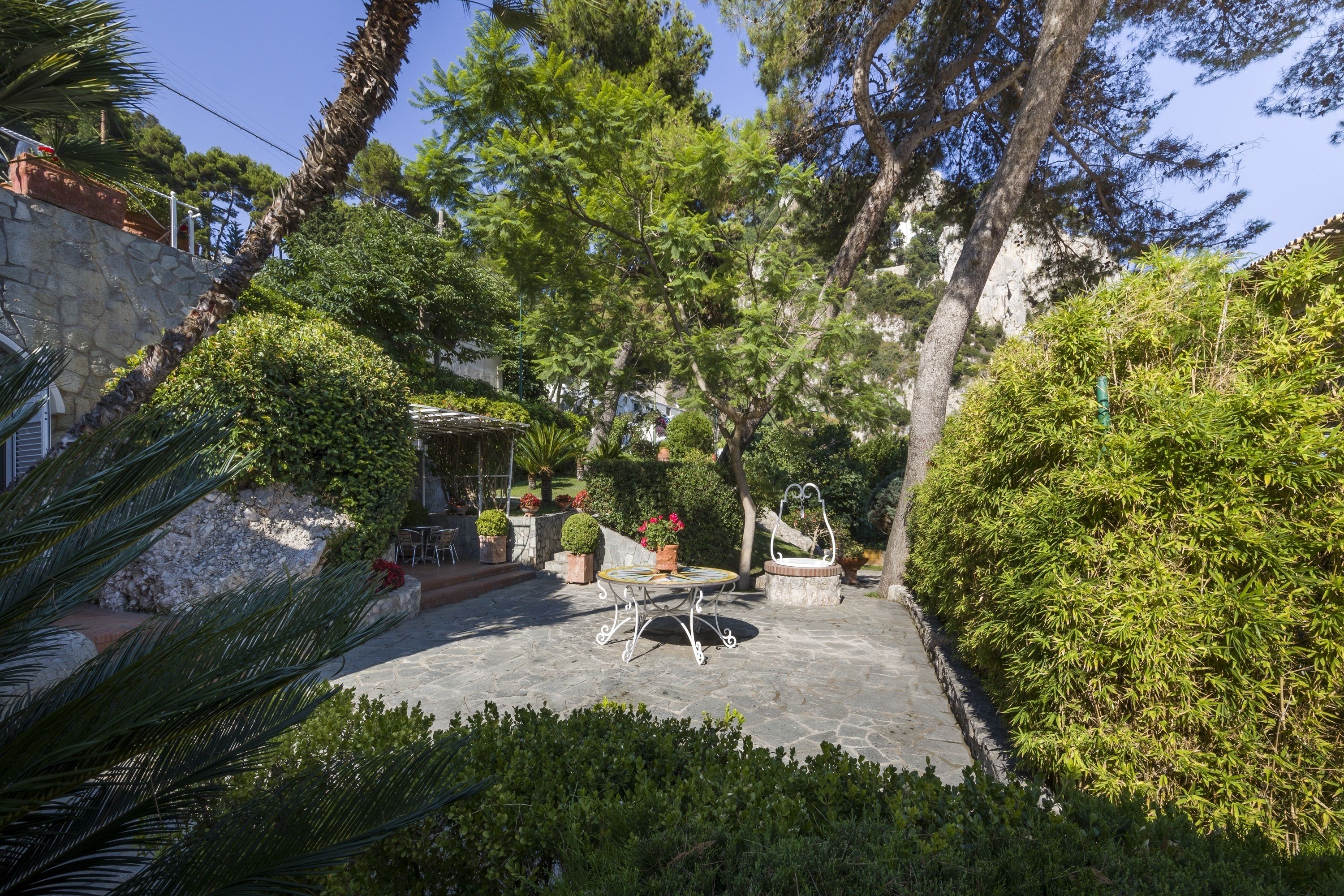 A courtyard with a stone table and chairs, surrounded by lush greenery and trees.