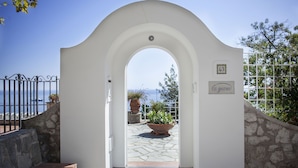 Una entrada con un arco blanco que conduce a un área pavimentada en piedra, con una maceta y un letrero que dice "la giara".