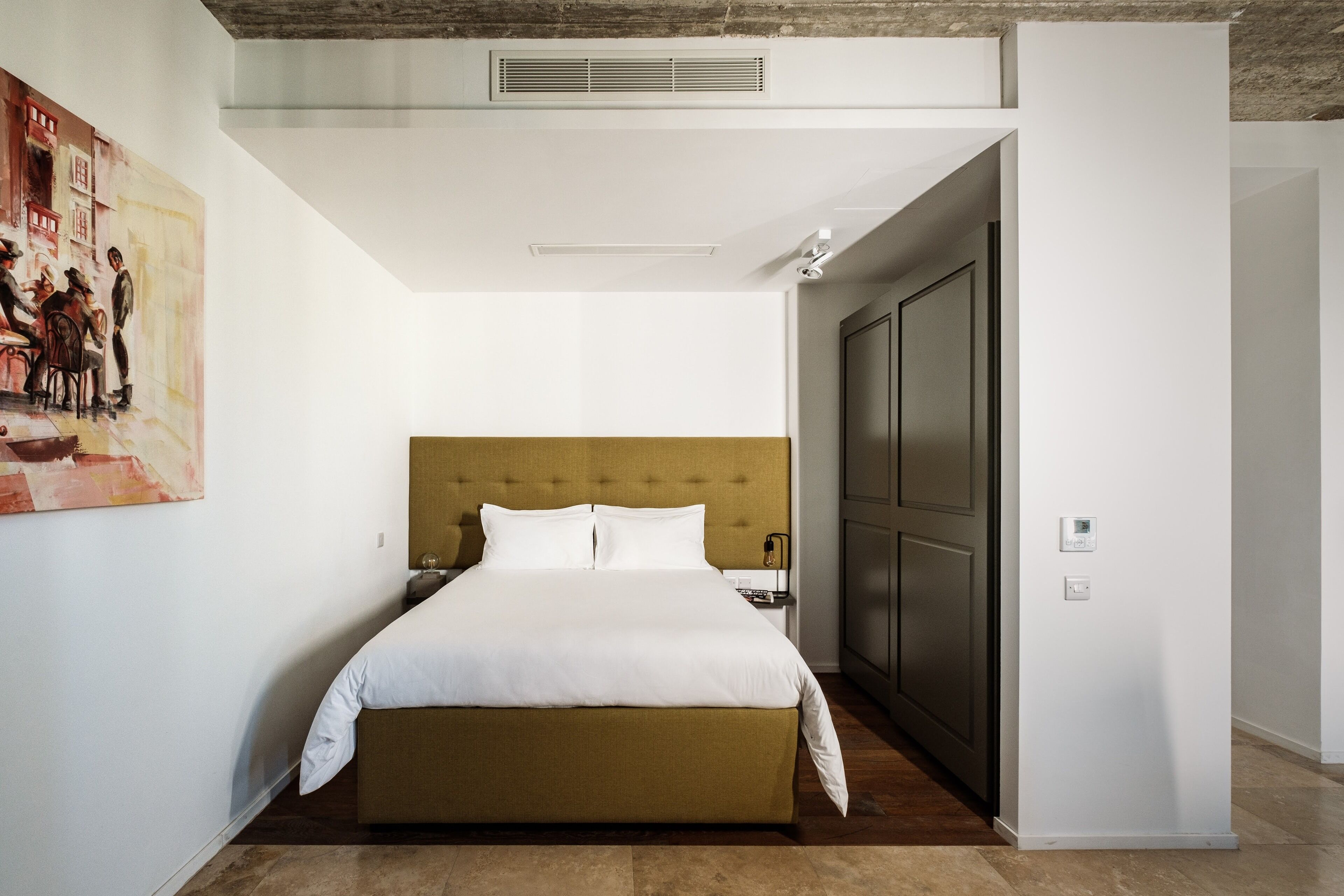Une chambre d’hôtel moderne avec un grand lit, une tête de lit, une armoire et un tableau au mur.