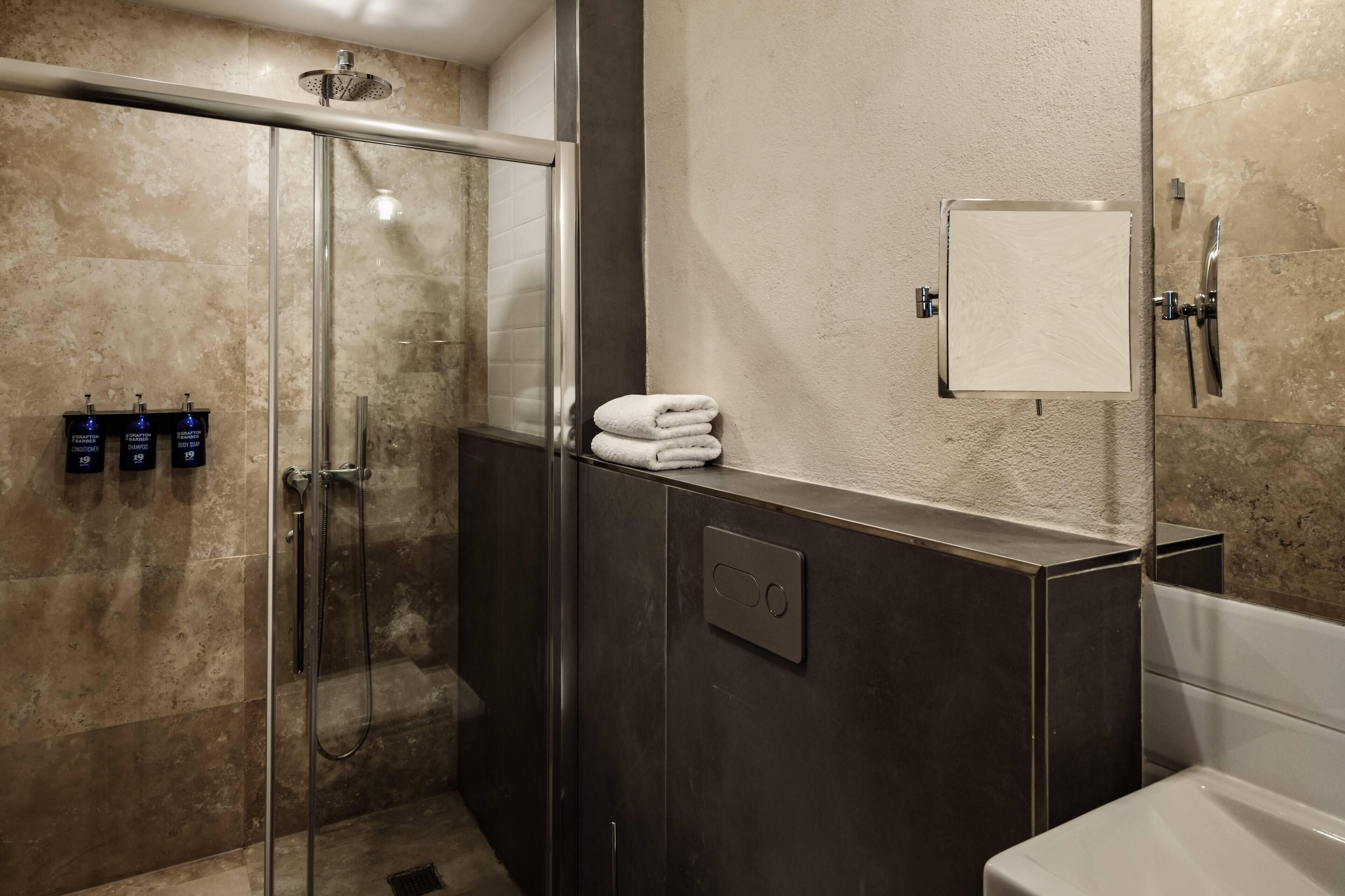 Un baño moderno con ducha de vidrio, una bañera blanca y un perchero con toallas dobladas.
