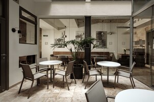 A modern indoor seating area with round tables and chairs, a potted plant, and a cityscape view through large windows.