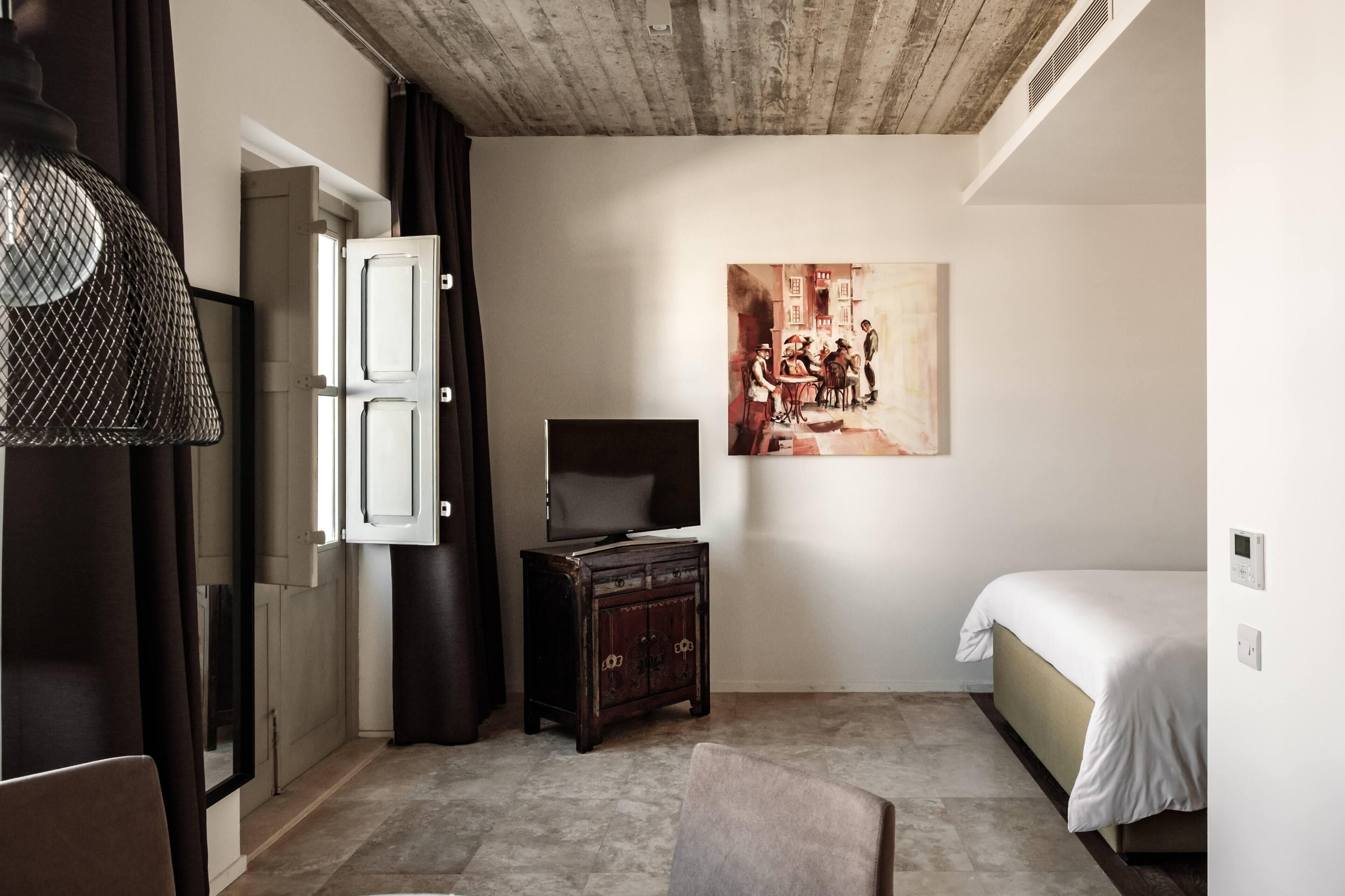 A bedroom with a bed, a dresser, a television, and a painting on the wall.