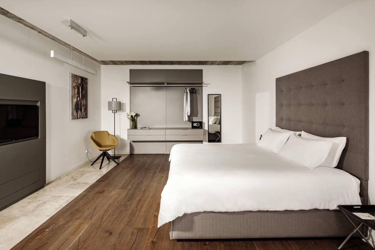 A modern bedroom with a large bed, a TV, a chair, a vanity, and a mirror.