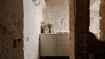 A narrow corridor with a white brick wall and a white door leading to a room with a white cabinet and a vase of flowers.