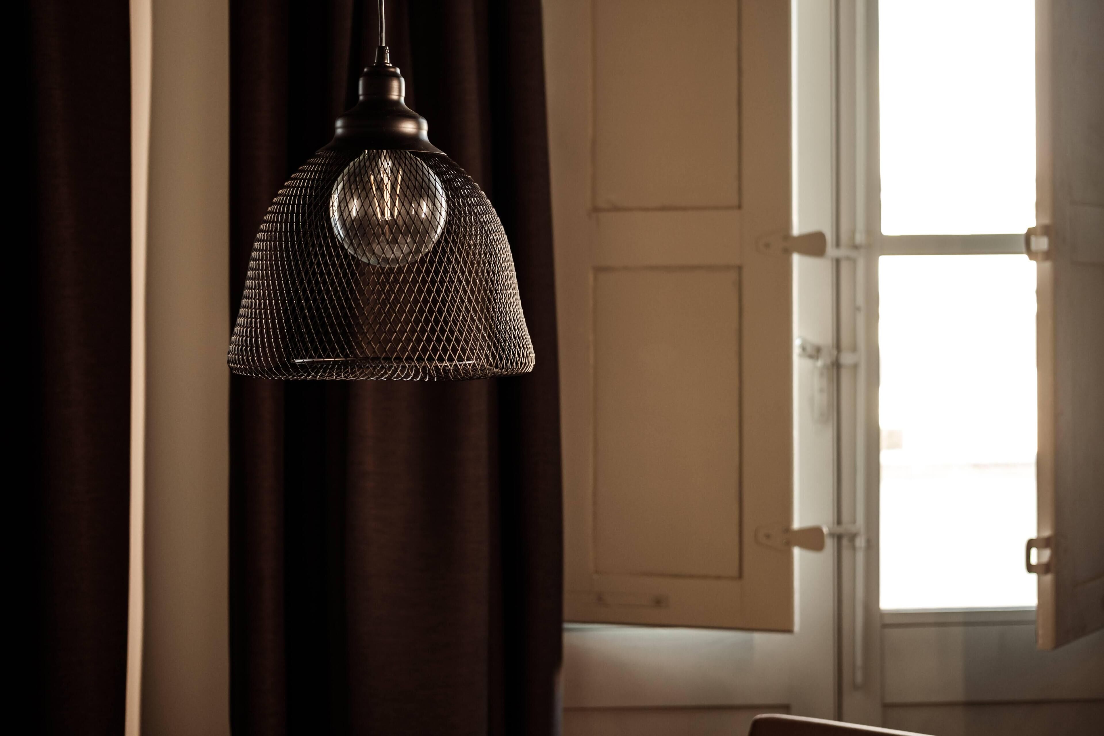 Una lámpara colgante con una pantalla texturizada en una habitación con ventana y cortinas.
