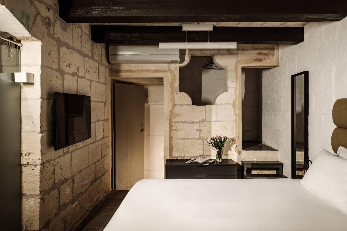 A bedroom with a stone wall, a flat-screen TV, a bed, a nightstand, and a mirror.