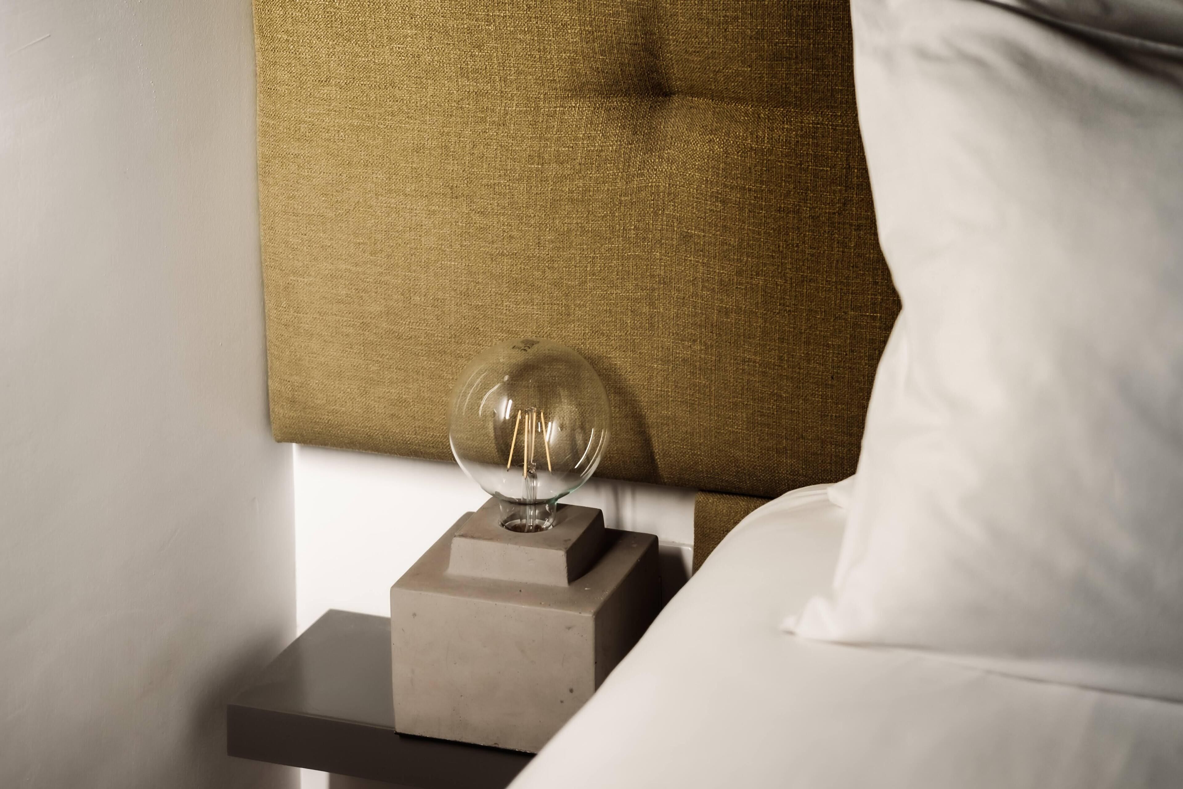A bed with a white pillow and a nightstand with a clear glass object on top.