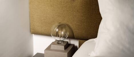 A bed with a white pillow and a nightstand with a clear glass object on top.