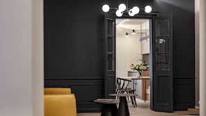 A modern interior with a dark wall, a yellow sofa, a black table, and a kitchen area in the background. - 19 Rooms (Valletta)