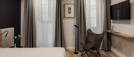 A modern hotel room with a bed, a desk with a chair, a mounted TV, and a large window with curtains.