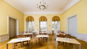 Una habitación amplia con varias mesas y sillas, un candelabro y ventanas grandes con cortinas.