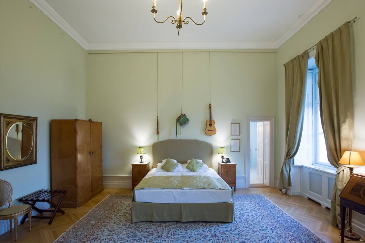 Un dormitorio con una cama grande, dos mesitas de noche con lámparas, un armario de madera, una guitarra en la pared y una ventana con cortinas.
