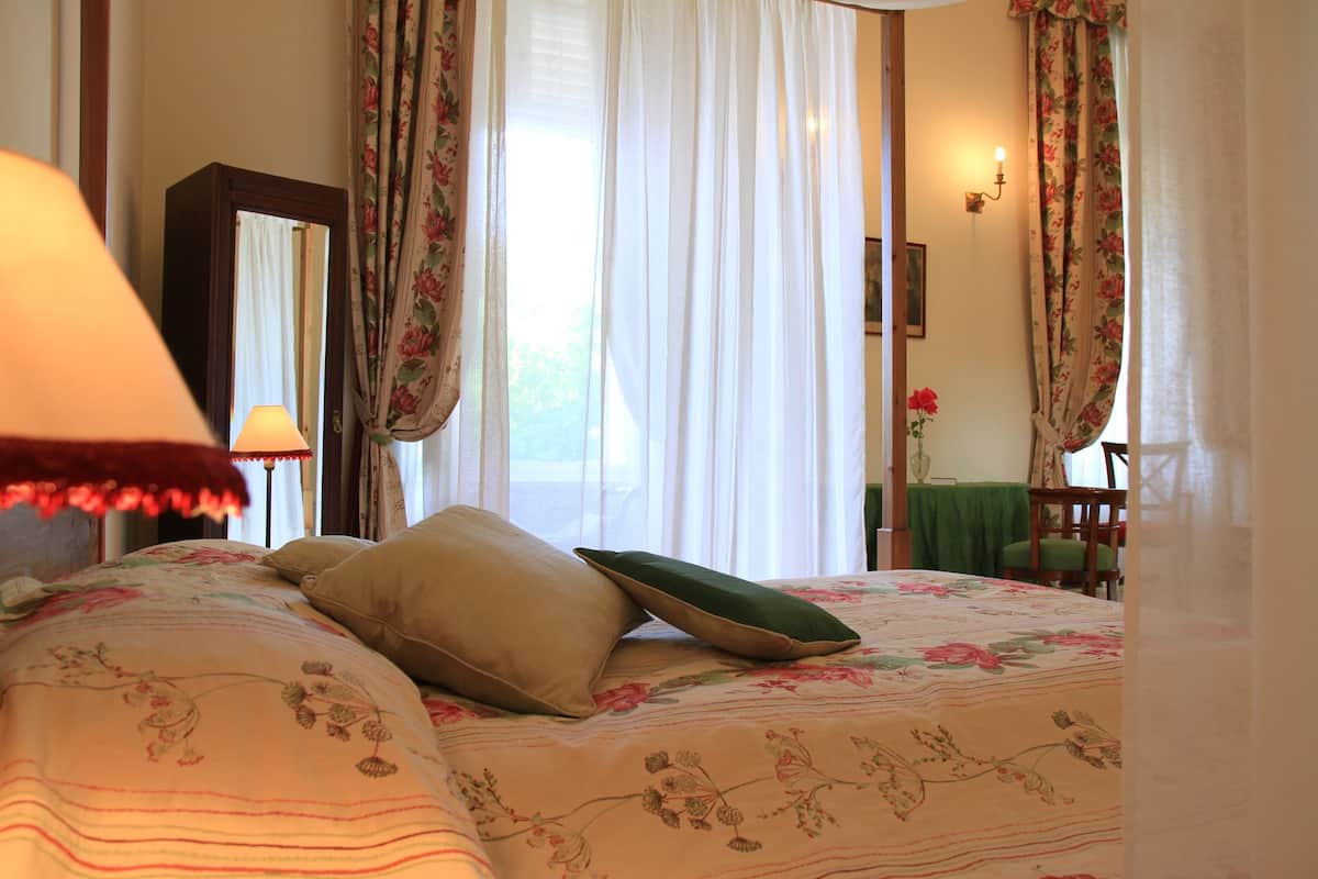 Un dormitorio con colcha estampada, un espejo, una lámpara y cortinas.
