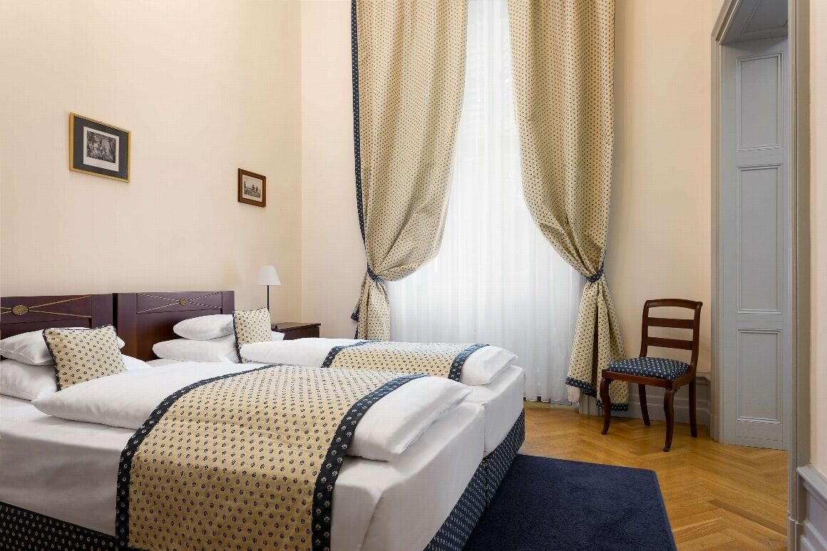 Une chambre d’hôtel avec un lit double, une chaise, un bureau et une fenêtre avec des rideaux.