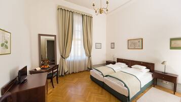 A neatly arranged bedroom with a bed, bedside tables, a desk with a chair, a mirror, and a chandelier.