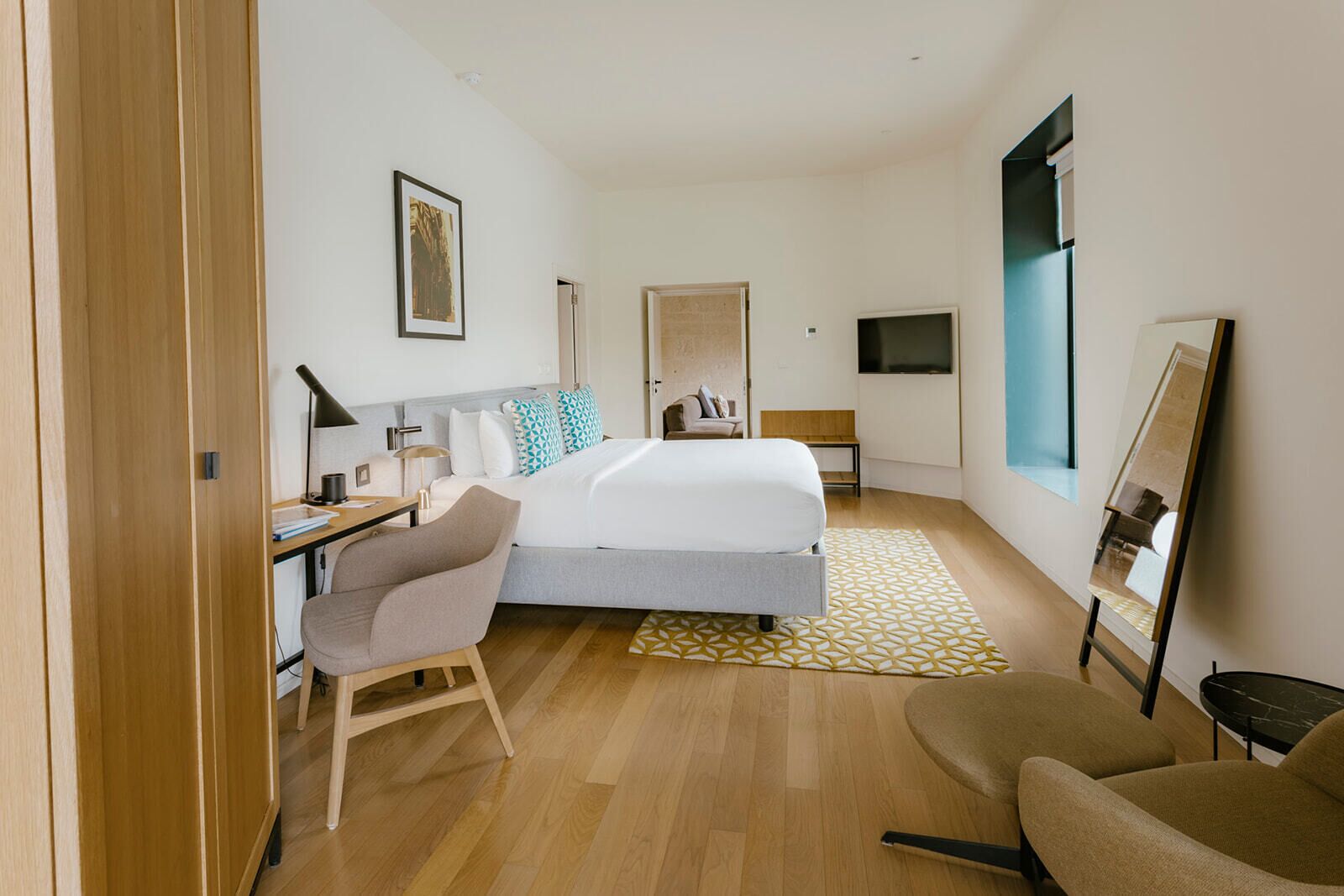 A modern hotel room with a bed, desk, chair, and a TV.