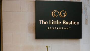 Un letrero de restaurante con logotipo y nombre, sillas blancas y una mesa con una bebida.