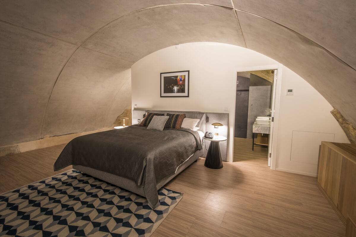 A bedroom with a bed, bedside table, lamp, and a geometric rug.